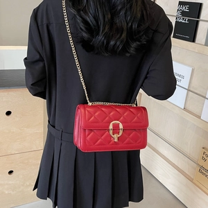 Detail of red quilted crossbody bag with gold horseshoe lock and chain strap on a model
