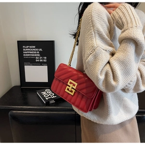 Détail d'un sac bandoulière rouge matelassé avec chaîne dorée et boucle métallique