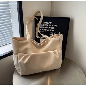 Close-up of cream faux leather tote bag with pleated pocket on a metallic table