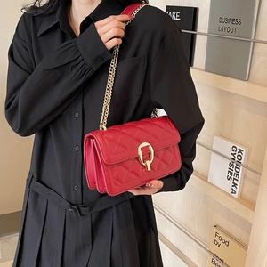 Detail of red quilted crossbody bag with golden chain and horseshoe clasp on model