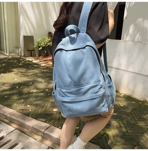 Side view of woman wearing a light blue denim backpack in a natural outdoor setting
