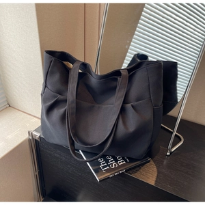 Detail view of large black canvas tote bag showing side pleats and front pocket design