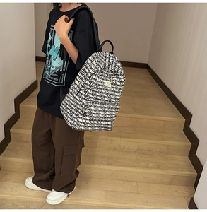 Side view of white backpack with black text print worn by model on wooden stairs
