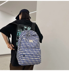 Detail of high-capacity beige backpack with blue text print on back of a model