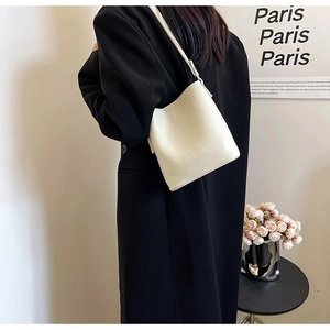 Borsa a secchiello beige minimalista indossata su cappotto nero per un look urbano