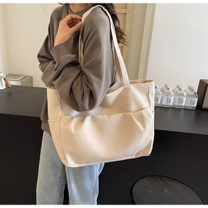 Close-up of cream white canvas tote bag with functional pleated front pockets on model