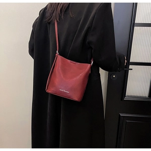 Dettaglio della borsa a secchiello in pelle bordeaux indossata su un blazer nero
