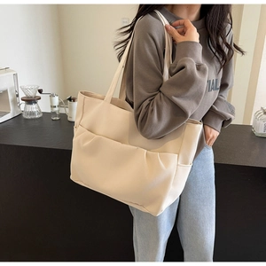 Detail of beige tote bag with pleated front pocket shown in a cozy cafe setting