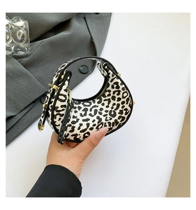 Close-up of leopard print crescent bag with gold hardware held by hand in stylish setting