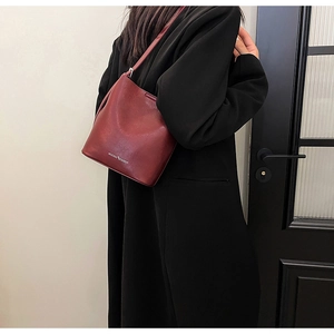 Vista laterale di una borsa a secchiello bordeaux in ecopelle lucida con logo stampato