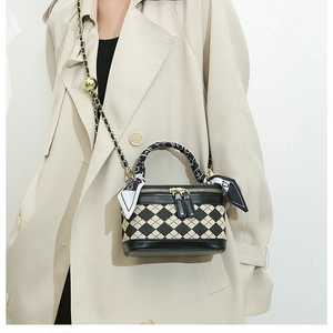 Close-up of a mini quilted box bag with chain strap and scarf-wrapped handle worn by model