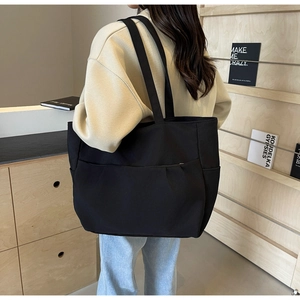 Detail of a large black canvas tote bag showing the layered front pocket and strap design