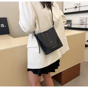 Borsa a secchiello minimalista in pelle nera indossata a tracolla con tracolla regolabile