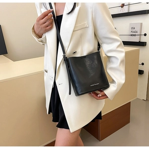 Dettaglio ravvicinato di una borsa a secchiello in pelle nera con logo bianco e tracolla