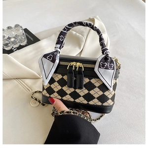 Detail of checkered box bag with scarf-wrapped handle and dual zippers on textured fabric