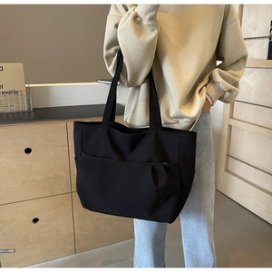Detail of a black large capacity tote bag with side pocket shown on a shoulder
