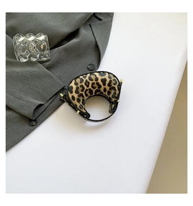 Detail view of mini leopard print crescent bag with golden studs on a white surface