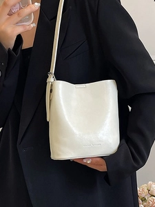 Borsa a secchiello bianco crema minimalista con tracolla regolabile su giacca nera