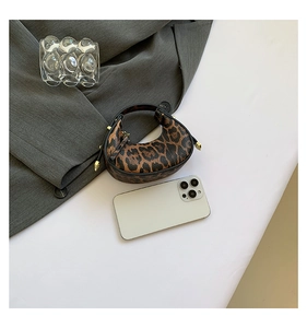Mini crescent leopard print handbag with metallic spikes next to a smartphone