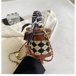 Detailed shot of cylinder bag with checkerboard pattern, gold chain and silk scarf handle