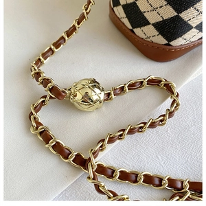 Close-up of golden metal ball buckle and braided chain strap on quilted handbag
