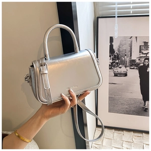 Detail showing the shiny silver patent leather texture and metal handle of the stylish bag