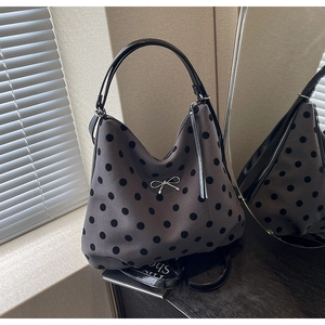 Détail du sac hobo gris à pois avec nœud argenté et poignée en cuir verni noir brillant