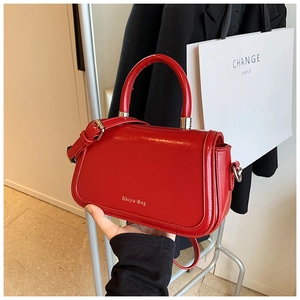 Detail of red glossy crossbody bag with gold lettering and silver hardware accents