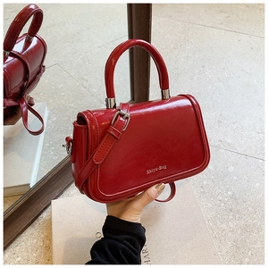 Detail of red glossy patent leather handbag with top handle and white logo branding