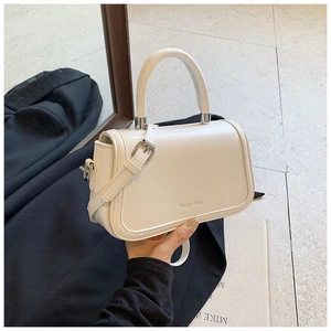 Detailed view of the creamy white leather handbag featuring adjustable strap and logo