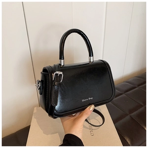 Detail of a black glossy leather handbag featuring silver Shiyu-Bag logo and top handle