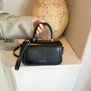 Detail of elegant black glossy crossbody bag with arched handle and white printed logo