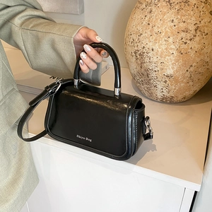 Close-up of a glossy black mini handbag with rigid curved handles and silver brand logo