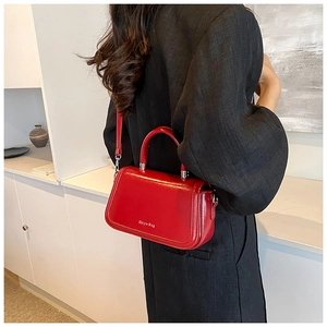 Detailed view of glossy red leather handbag worn crossbody by a model in a modern room