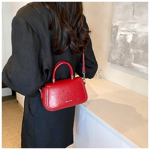 Glossy red handbag with top handle and shoulder strap shown in a modern lifestyle setting
