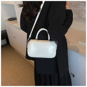 Close-up of white glossy PU leather handbag worn over a classic black suit jacket