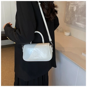 Close-up of a light grey leather crossbody bag showing the flap texture and silver hardware