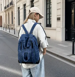 Outdoor shot showing back view of the dark blue denim backpack with contrast stitching