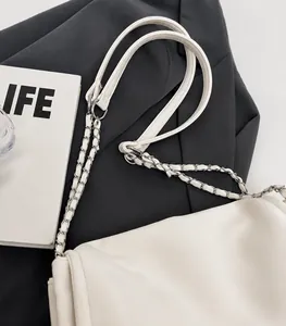 Detail of woven silver chain shoulder strap and leather texture on a white tote bag