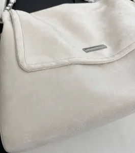 Close-up of beige suede crossbody bag with precise stitching and silver metal logo