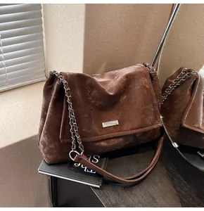 Detail of dark brown tote bag with vintage texture, chain strap, and silver logo plate