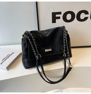 Detail of black suede shoulder bag with metallic logo plate and chain strap