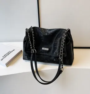 Close-up of distressed black leather texture and silver metal brand plaque on the flap bag