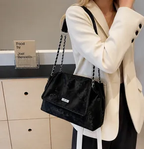 Close-up of black textured chain bag with silver logo plaque and metal strap detail