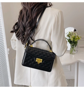 Détail du sac bandoulière matelassé noir avec fermoir doré sur fond de blazer blanc