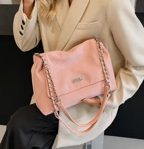 Detail of pink suede shoulder bag with woven chain strap and metal clasp on beige blazer