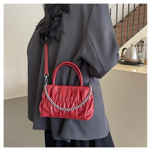 Detailed view of red pleated crossbody bag with silver chain worn by a female model