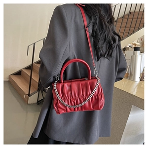 Detail of red pleated handbag with silver chain worn over a gray blazer