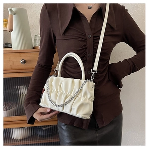 Close-up of off-white pleated crossbody bag with silver chain and top handle on model
