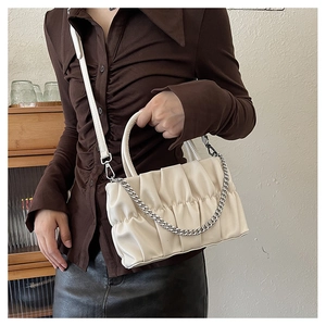 Creamy white pleated crossbody bag with silver chain and dual straps on brown shirt